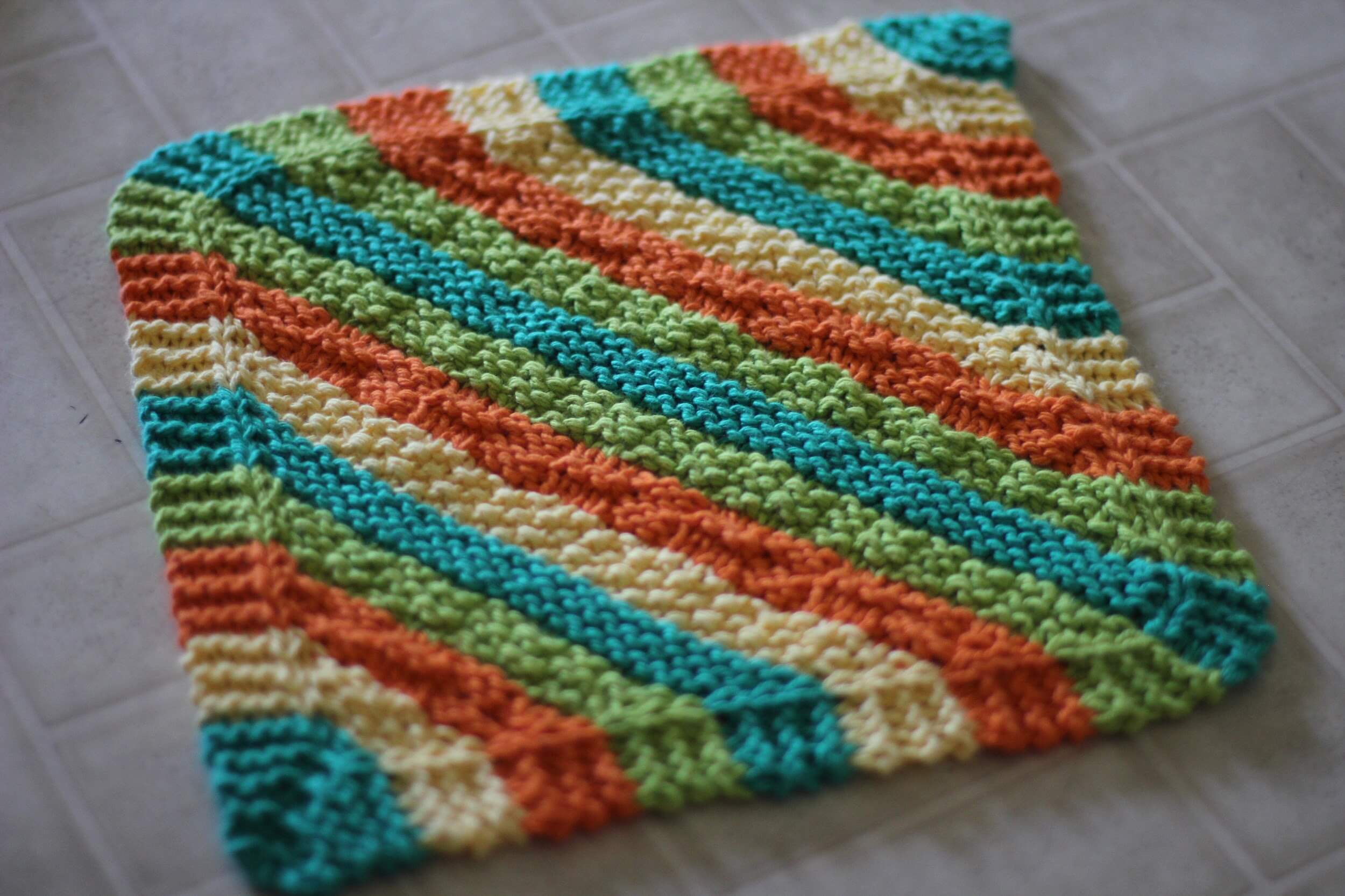 A knitted dishcloth with diagonal stripes in orange, green, yellow, and teal.