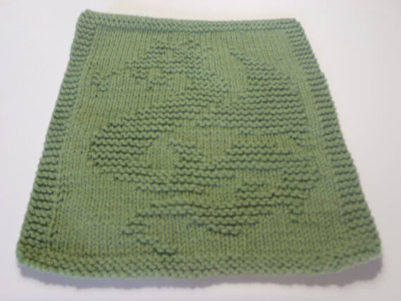 A green knitted dishcloth featuring a textured dragon design.