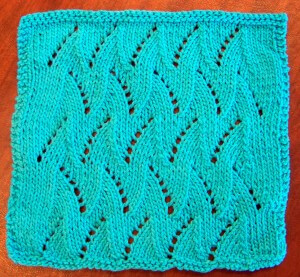 A teal knitted dishcloth with a lace pattern of diagonal eyelets.