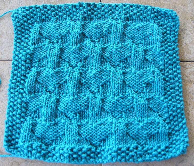 A blue knitted dishcloth featuring a repeating heart pattern.