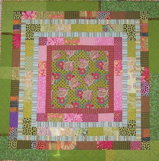 A quilt in different colours—green and pink—and patterns—paisley and flowers.